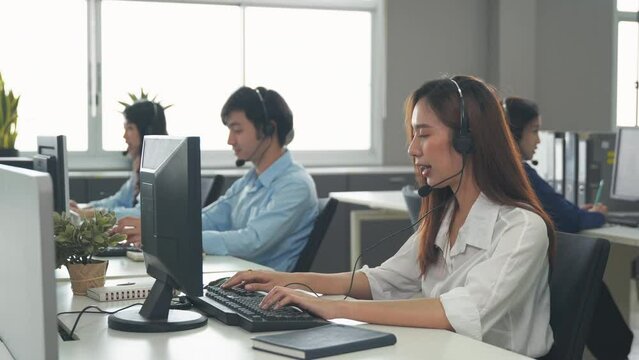 Call center young employee working with headset, Smiling customer support operator team at work surrounded by colleagues working in the office, Helpdesk customer services support agent concept