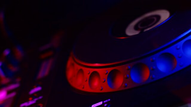 DJ's hand adjusts rotating jog on digital music console in neon light in nightclub, closeup. Concept of professional musical accompaniment