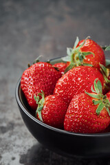 Fresh summer strawberries in a dark cup on an old rustic table, cope plan, selective focus. Background of ripe strawberries, vertical frame, delicious natural dessert