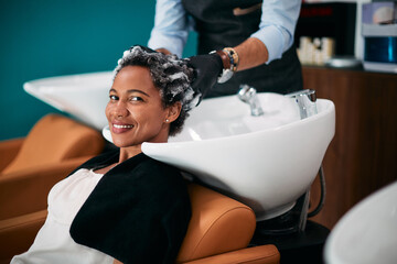 Happy black woman getting hair wash at hairdresser's and looking at camera.