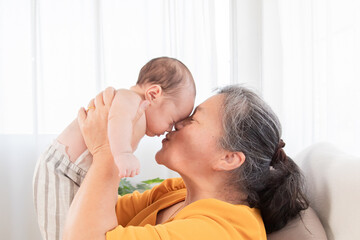 Side view grandmother and newborn baby play together at home, Grandma holding adorable infant in...