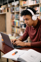 Young black student using laptop while studying at university library.