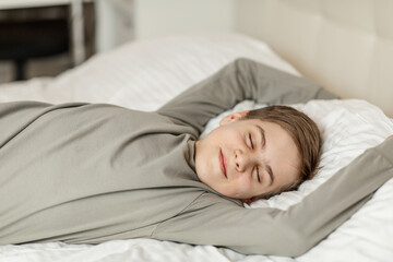 a teenage boy of European appearance is lying on the bed with his eyes closed