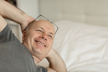 An adult man of European appearance in a gray T-shirt with a smile on his face, lying on the bed