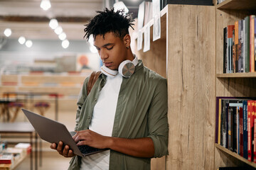 Young black student e-learning on laptop at university library.