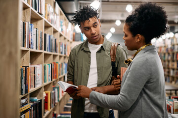 Young African American student talks to librarian at university library, - obrazy, fototapety, plakaty