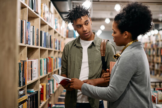 Young African American Student Talks To Librarian At University Library,