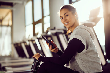 Happy athletic woman using mobile phone in gym and looking at camera.