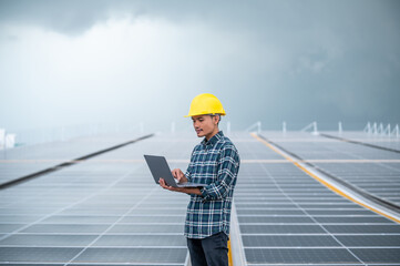 Asian engineer using computer working in solar power plant rooftop for control power system eco environmental