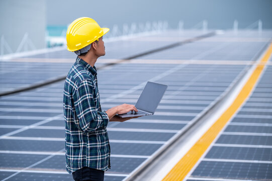 Asian engineer using computer working in solar power plant rooftop for control power system eco environmental