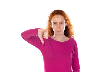 Discontent young redhead girl wearing pink t-shirt over white background shows disapproval sign, keeps thumb down