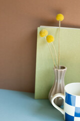 Notebook and cup and dry flower on blue desk. brown wall background