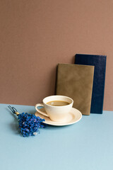 Notebook and cup of coffee and dry flower on blue desk. brown wall background