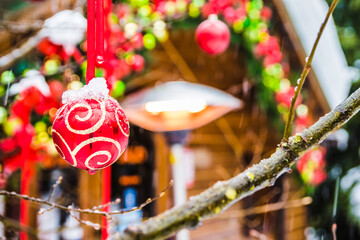 Red christmas ball hanging on tree branches covered with snow. Decorated tree in winter. Snowfall and Christmas toys on the street