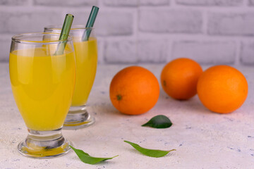 Orange juice in tall glasses and fresh oranges.