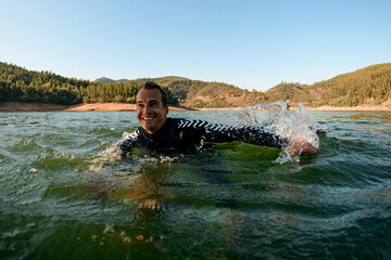 close-up of cheerful man in wetsuit floats on the river water.