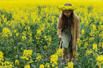 Fototapeta premium a cute six-year-old girl in a khaki cotton dress walks through a rapeseed field 