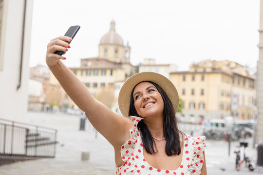 Happy woman taking selfie through smart phone in city