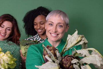 Happy multiracial friends with fresh raw vegetables standing against green background