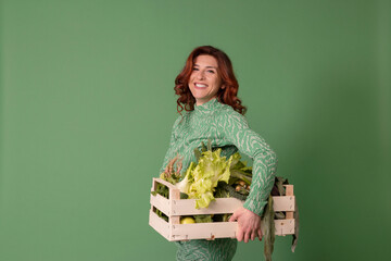 Smiling woman holding wooden crate with vegetables against green background