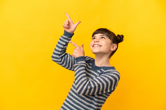 Little caucasian girl isolated on yellow background pointing with the index finger a great idea