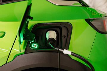 Green electric car being charged by plug at charging station
