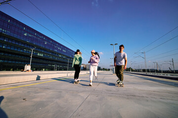 Three excited teenagers spend time in the urban exterior. They are running and skateboarding.