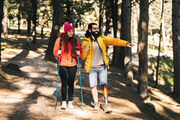 Happy disabled man pointing away by woman walking with hiking pole in forest