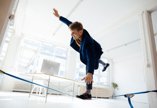 Happy businessman slacklining in office