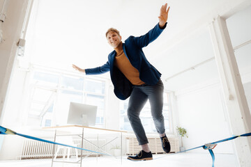 Happy businessman balancing on tightrope in office