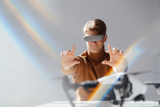 Businessman wearing virtual reality simulator making finger frame towards drone in office