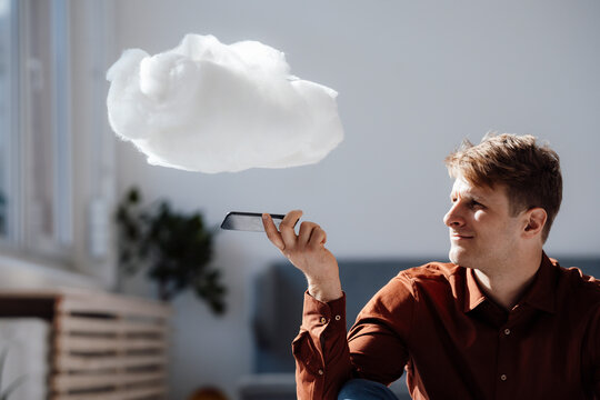 Businessman holding mobile phone under levitating cloud network in office