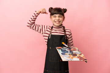 Little artist girl holding a palette isolated on pink background doing strong gesture