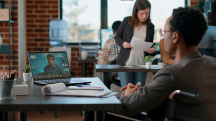 Office worker in wheelchair meeting with colleague on videocall conference, talking about business project. Professional employee using online teleconference call to have conversation on laptop.