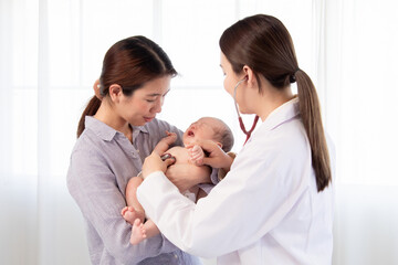 Asian woman doctor using stethoscope examining  on newborn baby in mother's arms. Mom holding...