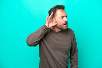 Middle age caucasian man isolated on blue background listening to something by putting hand on the ear
