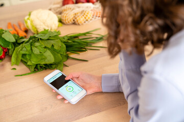 Woman using mobile app by vegetables at dining table