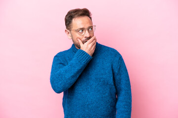 Middle age caucasian man isolated on pink background doing surprise gesture while looking to the side