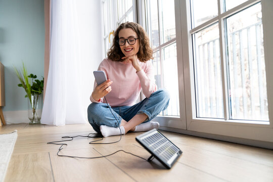 Smiling businesswoman using mobile phone sitting on ground at home