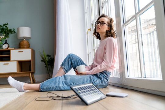 Thoughtful freelancer with coffee cup leaning on window