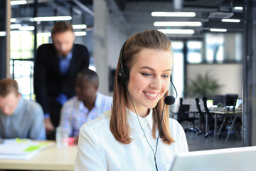 Fototapeta premium Portrait of call center worker accompanied by her team. Smiling customer support operator at work.