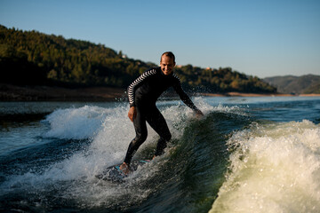 Cheerful man in wetsuit on wakesurf riding down the splashing wave