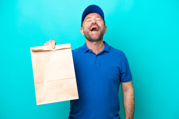 Middle age man taking a bag of takeaway food isolated on blue background laughing