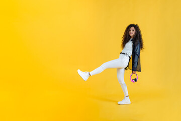 Fototapeta na wymiar Young woman taking long step while walking in studio shot with yellow background