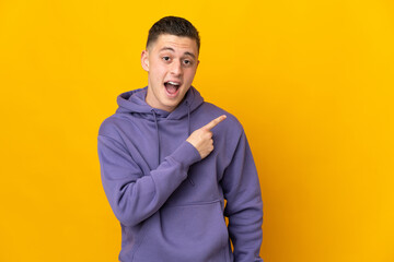 Young caucasian man isolated on yellow background surprised and pointing side