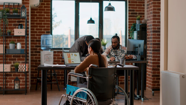 African american man helping woman in wheelchair with transportation, entering office job. Person with impairment working on business charts development, planning financial strategy. Tripod shot. - Powered by Adobe