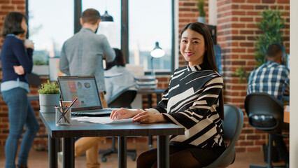 Portrait of asian HR employee analyzing cv information of candidates before attending job interview and discussing employment. Woman looking at resume files and smiling in company office.