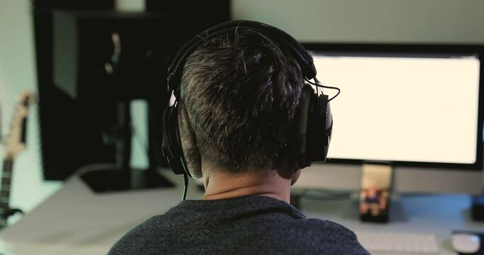 Music producer seen from behind listening with headphones to the project he is currently working on at his home studio