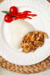 Close-up of Pork Goulash with heart-shaped rice, peppers and tomatoes on a white plate.