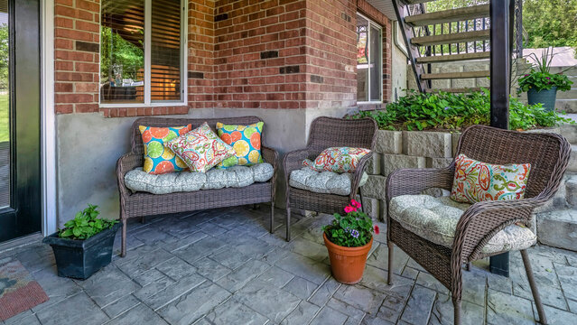 Panorama Woven couch and armchairs on an outdoor patio under the deck of a house with bricks